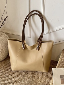 Large beige leather tote bag with brown handles in a minimalist home interior setting
