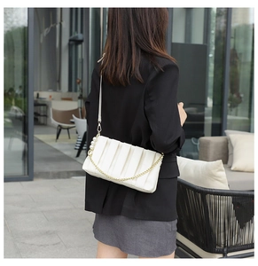 Detail of white pleated bag with gold chain and pearls shown on a female model shoulder