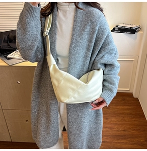 Detail of a creamy white crescent bag with wide shoulder strap and silver buckle