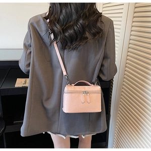 Sac bandoulière rose à motif autruche porté sur un blazer gris avec une poignée