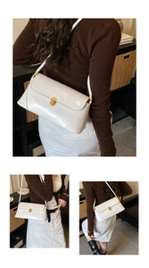 Detail of white glossy leather baguette bag featuring a gold metal twist-lock clasp
