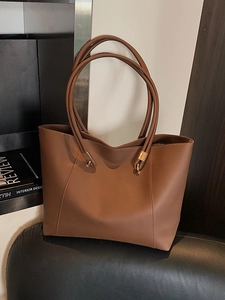 Brown leather tote bag with long shoulder straps and gold rings on a black bench