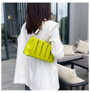 Detail of neon green pleated shoulder bag with elegant pearl and gold chain strap