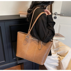 Detail of a brown leather tote bag featuring contrast stitching and silver metal buckles