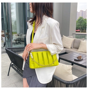 Detail of neon green pleated square bag featuring pearl and gold chain decorations
