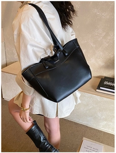 Close-up of black leather tote bag featuring a polished metal logo and spacious interior