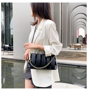 Detail of black pleated shoulder bag with gold chain and pearl charm on a model
