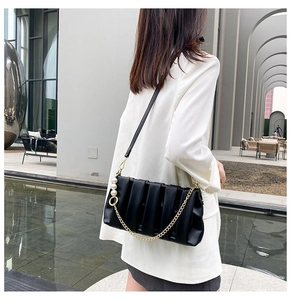 Detail of black pleated crossbody bag with gold chain and large pearl ornament