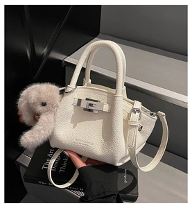 Detail of white lychee leather bucket bag with silver lock and plush bunny charm