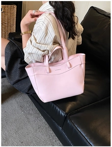 Close-up of pink leather tote bag with embossed lettering on a black leather sofa