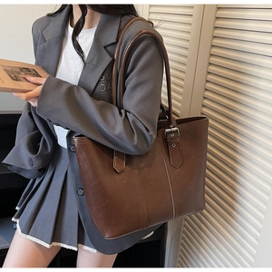 Close-up of dark brown vintage tote bag featuring silver buckles and smooth PU leather texture