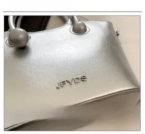 Λεπτομέρεια της ασημένιας τσάντας με ανάγλυφη υφή και μεταλλικό λογότυπο JFYDS