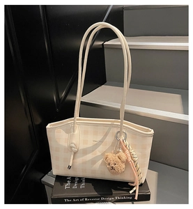Detail of a beige plaid tote bag with a plush bear charm and slender shoulder strap