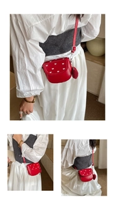 Détail du sac à selle rouge avec broderie cœur et charme de pompon en peluche