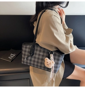 Detail showing high-capacity grey plaid tote bag with teddy bear charm on model