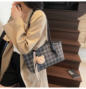 Close-up of a checkerboard tote bag with bear charm and logo on a leather shoulder strap