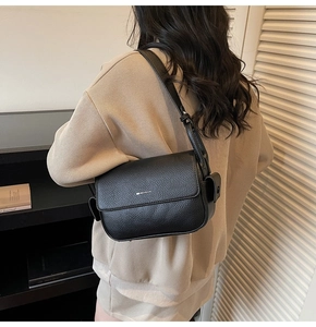 Detail of a black litchi leather shoulder bag with a metal hook and adjustable strap
