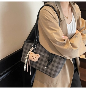 Detail of checkered tote bag with plush bear charm and woven tassel accent worn by model