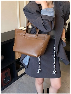 Brown leather tote bag detail showing trapezoidal structure and double handles on model