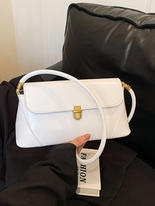 Minimalist white patent leather underarm bag with gold vintage clasp on a black sofa
