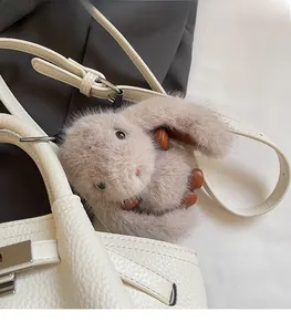 Close-up of a cute fluffy light brown rabbit keychain on a white lychee leather handbag