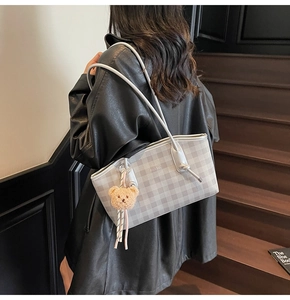 Detail of grey checkerboard tote bag with plush bear charm worn on black leather jacket