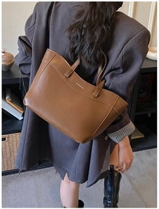 Detail view of large brown leather tote bag with gold logo and dual handle straps