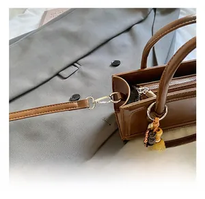 Detailed close-up of premium metal hooks and wooden bead charm on a brown leather handbag