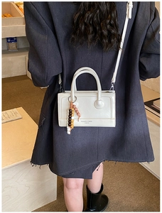 Close-up of a cream-white square handbag with beaded charm and leather strap detailing