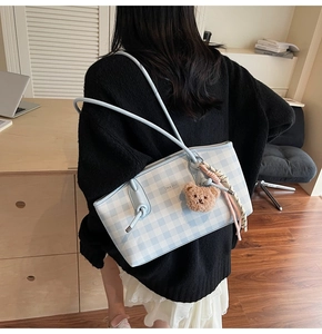 Detail of blue plaid tote bag with plush bear charm and colorful woven strap handle
