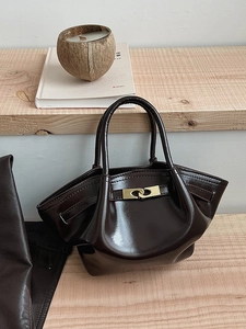 Elegante mokkabraune Lackleder-Handtasche mit Goldschließe auf minimalistischen Holzstufen