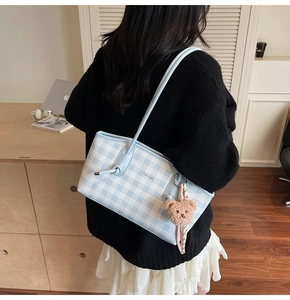 Detail of blue plaid tote bag with bear charm worn by a model in a cozy setting