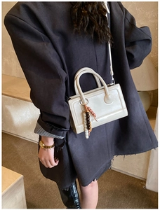 Detail view of cream polished leather handbag with elegant wooden bead charm and long strap