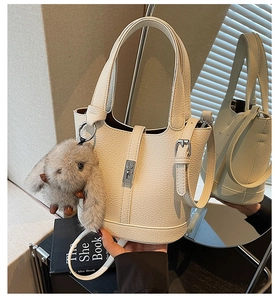Detail of white litchi leather bucket bag featuring a metal lock and plush rabbit charm