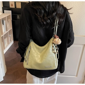 Gros plan du sac hobo en cuir souple vert clair avec poches zippées et ours peluche