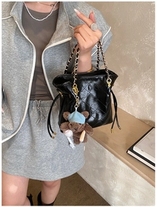 Detail of black quilted bucket bag with gold chain strap and cute bear plush charm