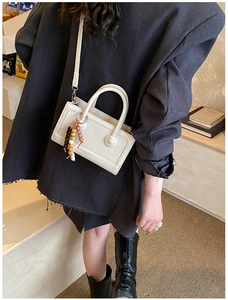 Detail of a vintage cream-colored crossbody bag with decorative wooden beads and slim strap