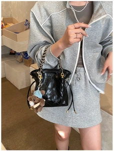 Detail of black quilted bucket bag with gold chain handle and brown teddy bear charm