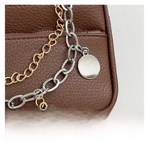 Detail of brown litchi grain leather texture with gold and silver chain ornaments