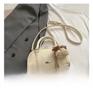 Detail of off-white crossbody bag with plush puppy charm on a soft bed setting