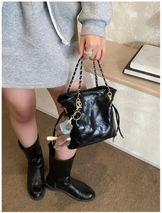 Detail of black quilted leather handbag featuring chain handle and cute bear charm