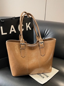 Brown large capacity leather tote bag with silver buckles on a dark leather sofa