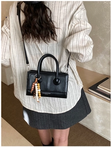 Close-up of black leather box bag with wooden bead charm and long shoulder strap