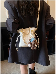 Detail of white quilted bucket bag with golden chain and cute brown teddy bear charm