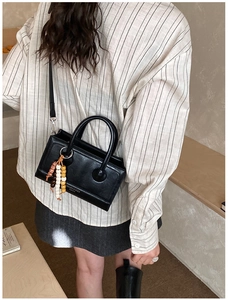 Detail of vintage black crossbody bag with beaded charm on a striped shirt model