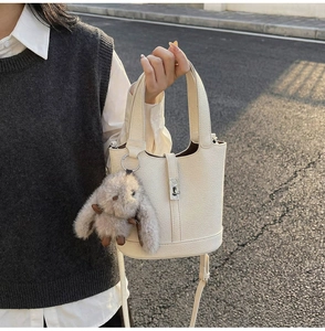 Close-up of cream leather bucket bag with h-shaped lock and grey bunny charm detail