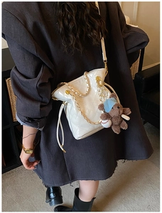 Close-up of a white quilted crossbody bag with a gold chain strap and cute bear charm