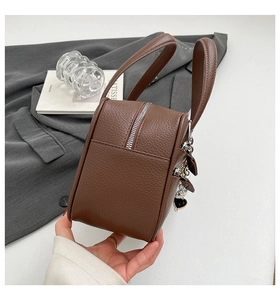 Detail view of brown pebbled leather briefcase featuring silver zipper and heart charm