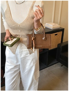 Detail of a brown vintage square handbag with colorful bead pendant and top handle