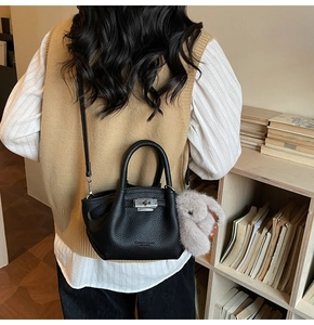 Detail of black pebbled leather bucket bag with silver lock and grey faux fur keychain
